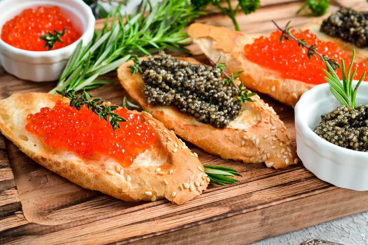 Open faced sandwiches topped with caviar, herbs, and spreads on a wooden board