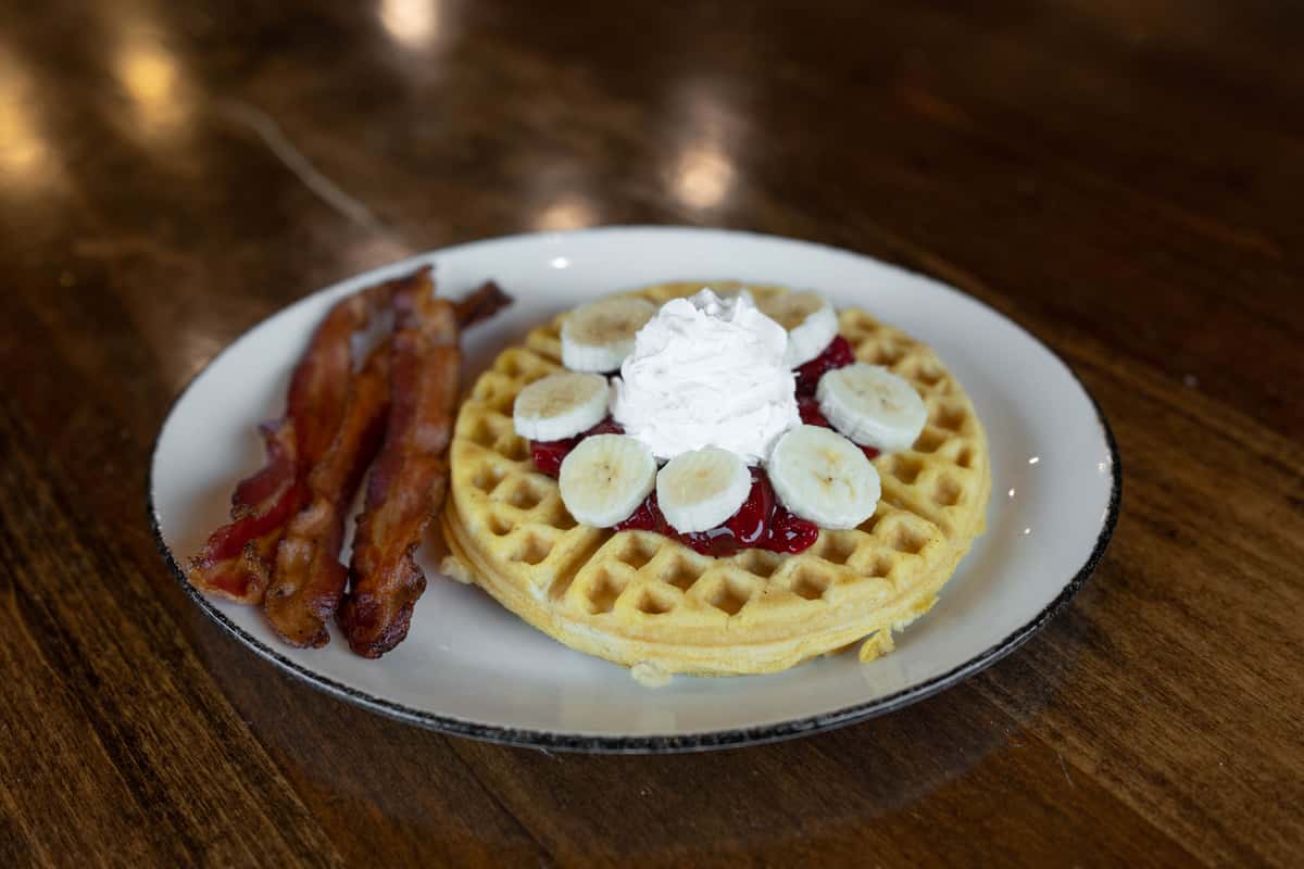 Waffles with bananas, jam, whipped cream, and a side of bacon