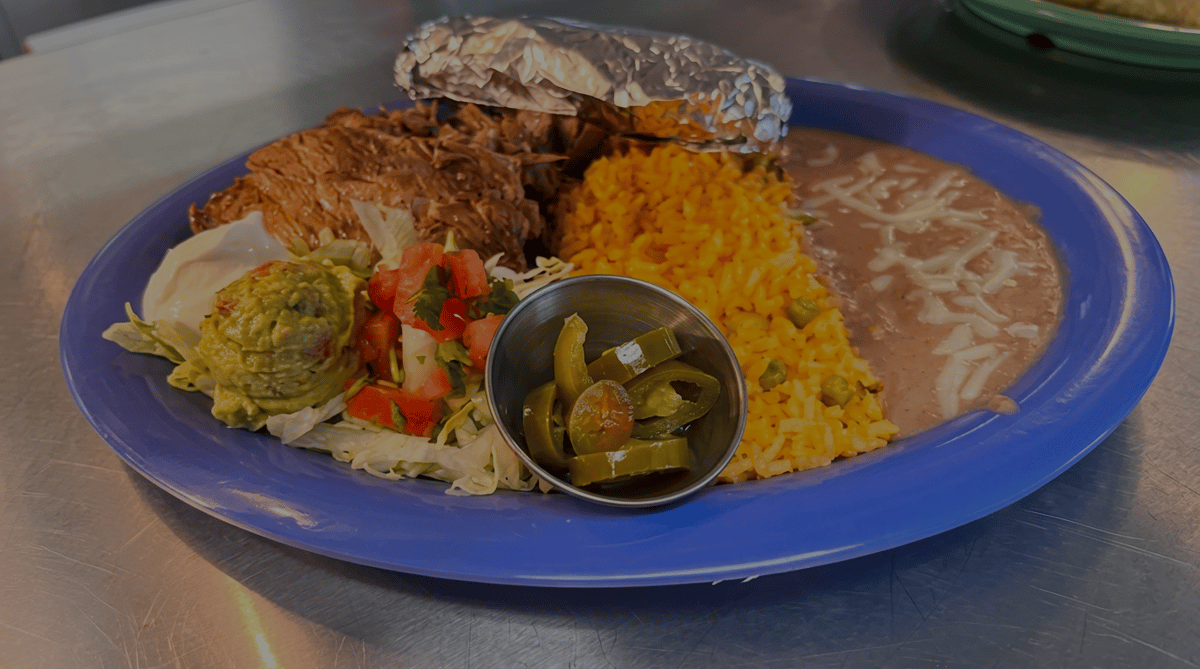 Grilled carne asada served with Mexican rice, refried beans topped with melted cheese, a baked potato, fresh guacamole, pico de gallo, jalapeños, and a crisp side salad at El Cazo Mexican Restaurant.