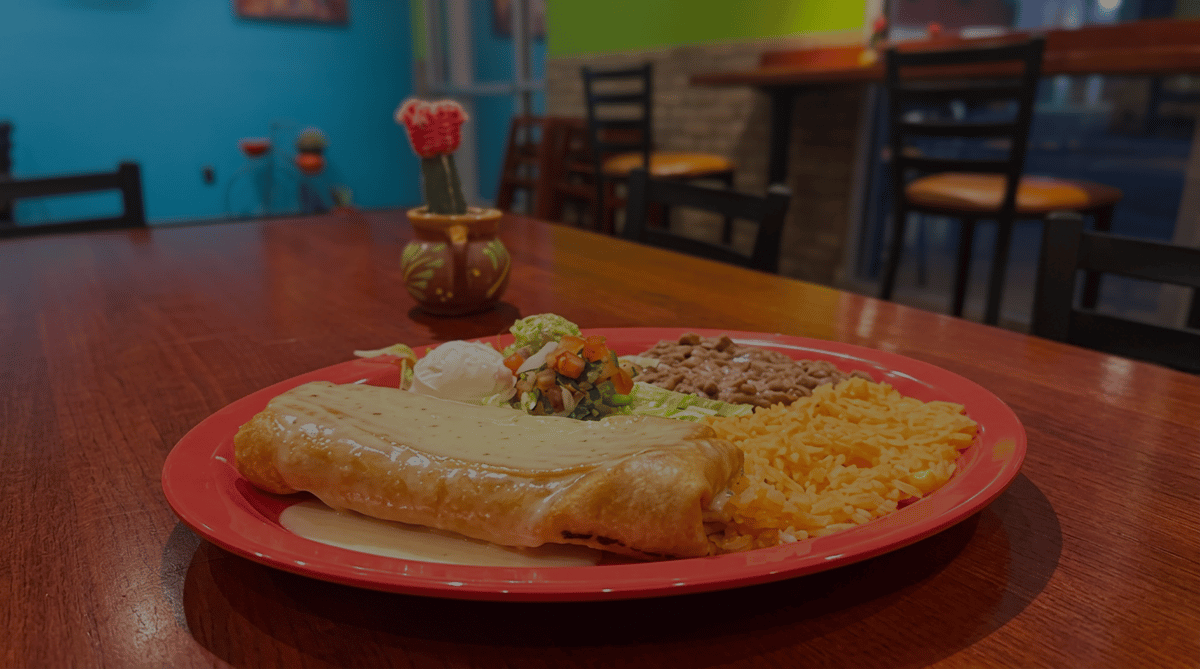 Smothered burrito topped with creamy cheese sauce served with Mexican rice, refried beans, sour cream, and fresh pico de gallo at El Cazo Mexican Restaurant.