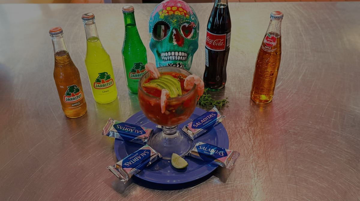 Mexican shrimp cocktail garnished with fresh avocado, shrimp, and lime, served with traditional crackers and assorted Mexican sodas at El Cazo Mexican Restaurant.