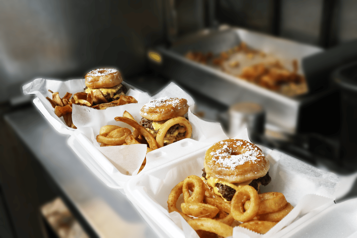 Hangry's Grill's Three donut burgers with onion rings are nestled in styrofoam containers.
