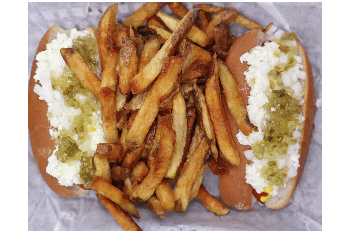 Hangry's Grill's two hot dogs topped with a creamy sauce and green relish, served with a generous pile of french fries.