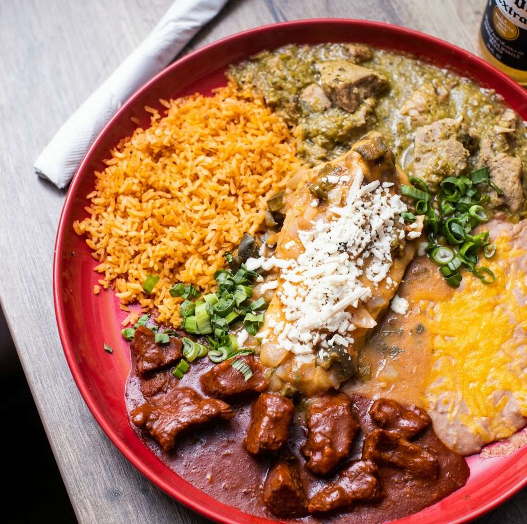 Red plate with Mexican combination dinner: rice, chile verde, chile relleno, carne guisada, and refried beans.