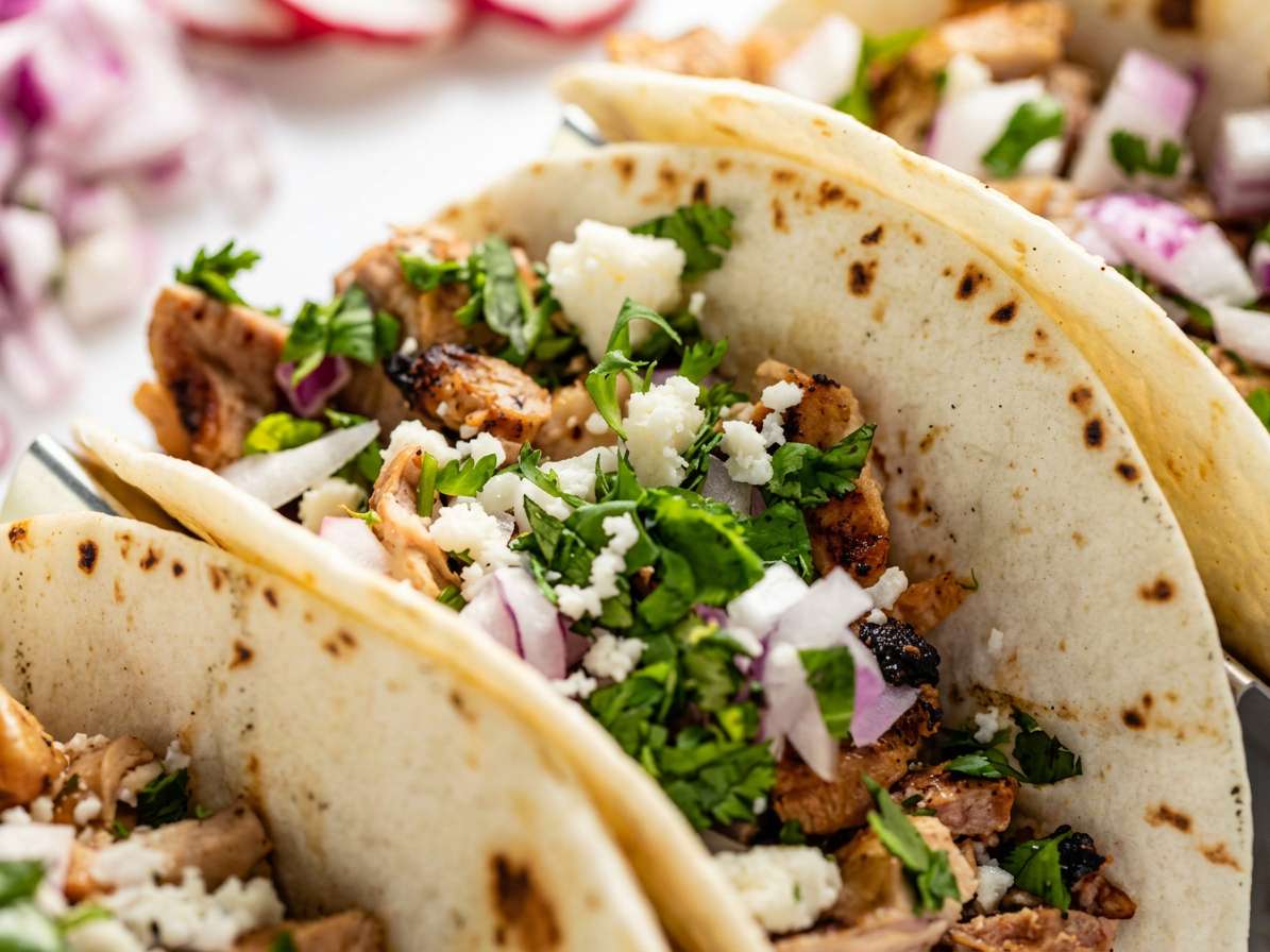 Mexican tacos filled with grilled meat, cilantro, crumbled white cheese, and diced red onion.
