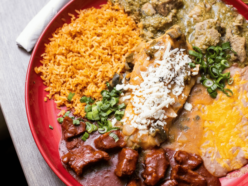 Red plate with Mexican combination dinner: rice, chile verde, chile relleno, carne guisada, and refried beans.
