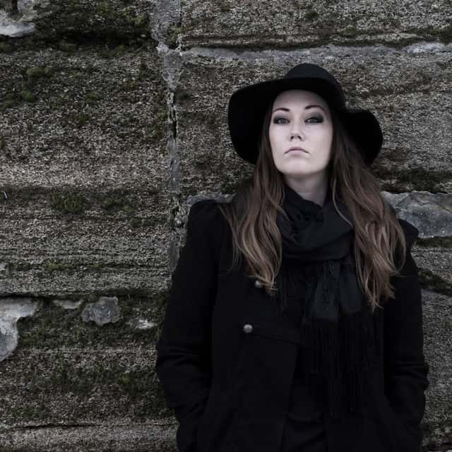 Portrait infront of a brick wall wearing black jacket and hat