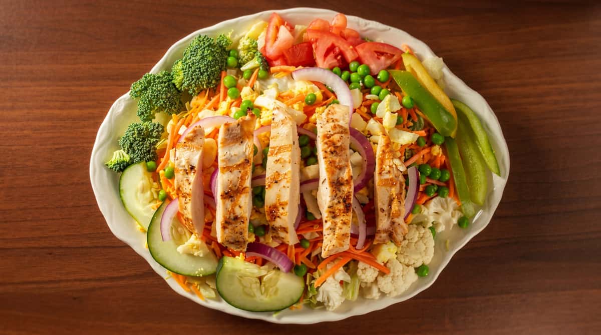 Grilled chicken salad with mixed greens, carrots, peas, tomatoes, cucumber, red onion, and broccoli florets.