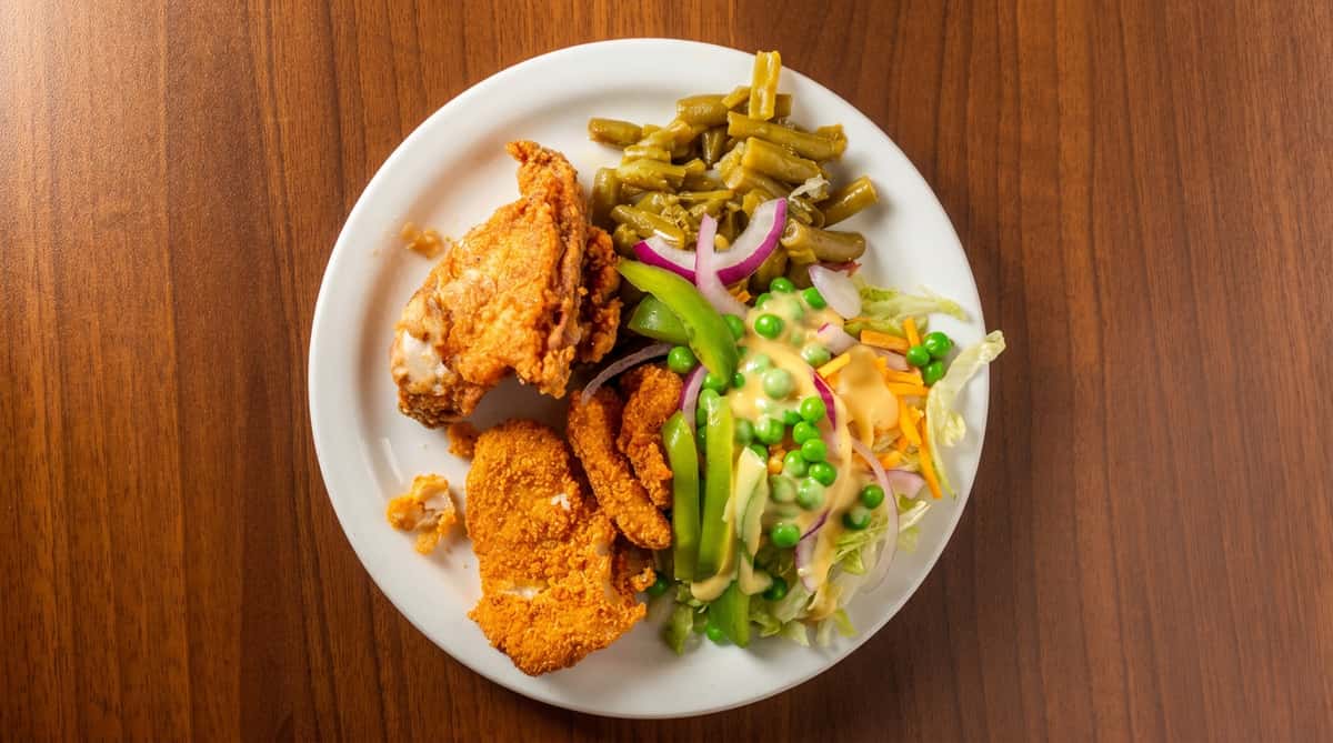 Fried chicken, fried fish, green beans, and a salad with lettuce, peas, shredded carrots, red onion, and dressing on a white plate.