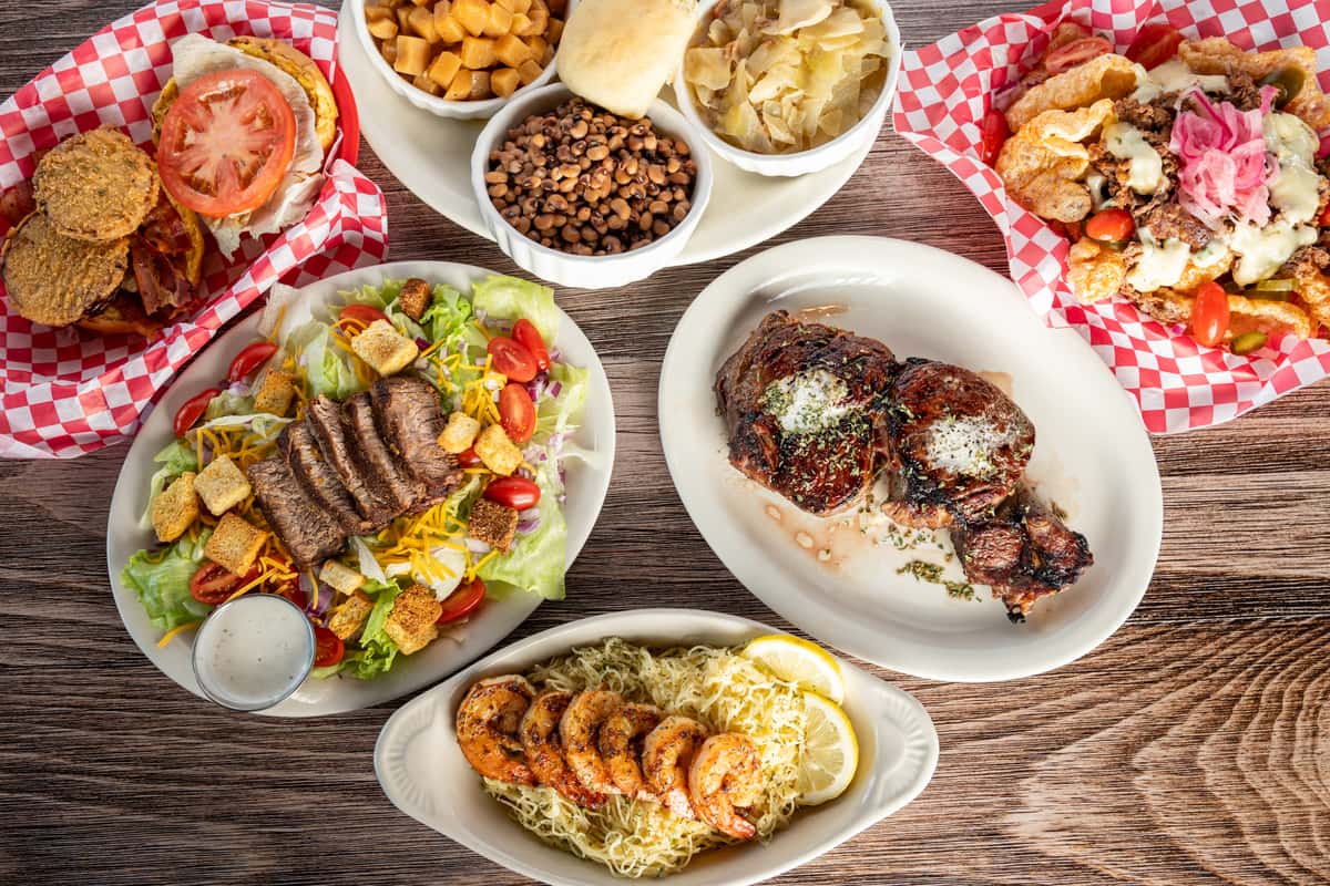 Overhead view of a table spread at Woody's with a grilled steak salad, glazed ribs, grilled shrimp over rice, fries, and dipping sauces