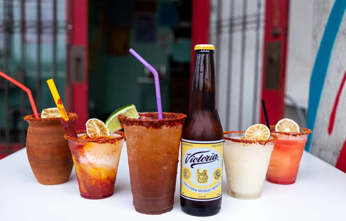 Colorful chili-rimmed Mexican-inspired drinks and a Victoria beer bottle from Milagro Tacos Cantina, displayed in a vibrant, festive setting.