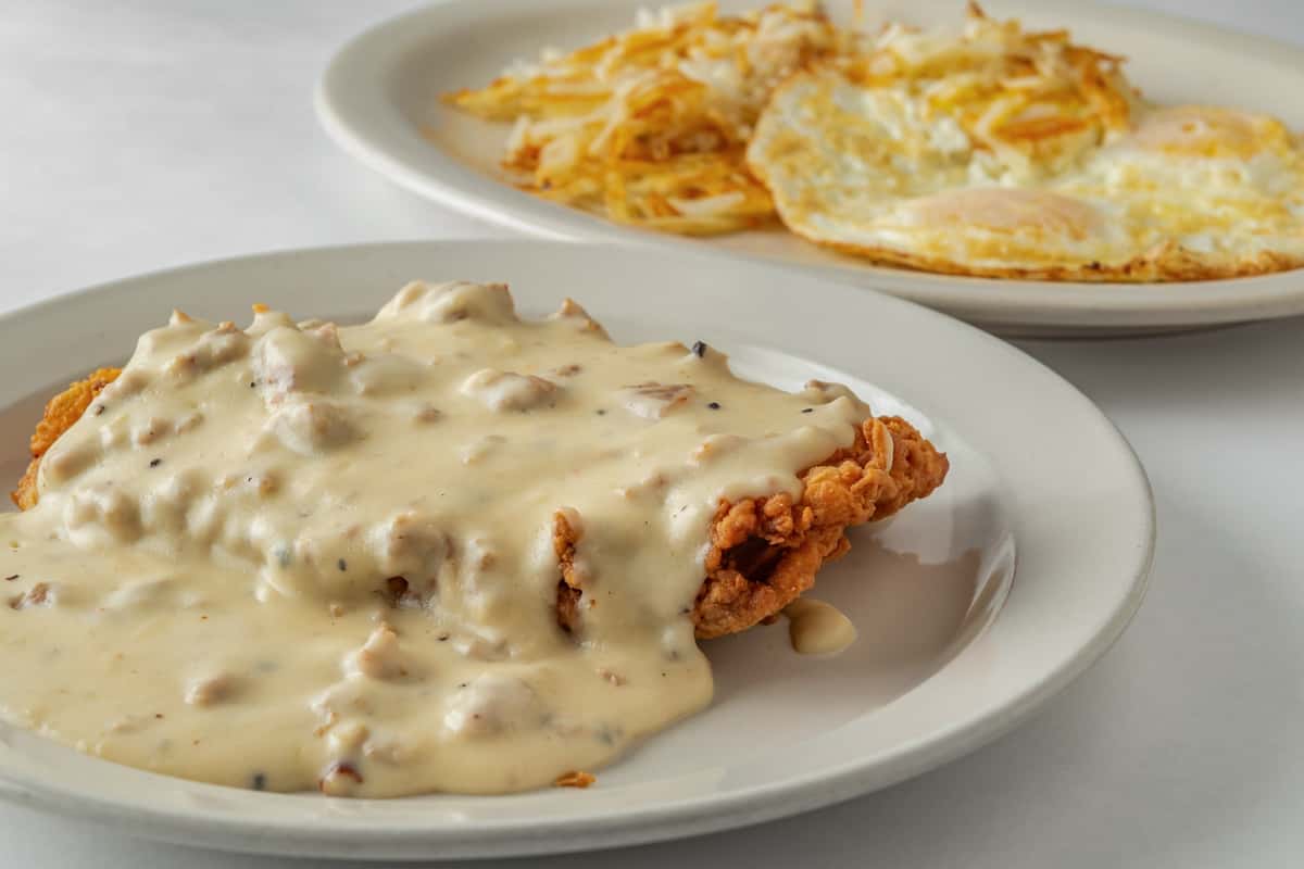 Southern-style chicken fried steak smothered in creamy country gravy, served with a side of hash browns and sunny-side-up eggs — a hearty American breakfast classic.