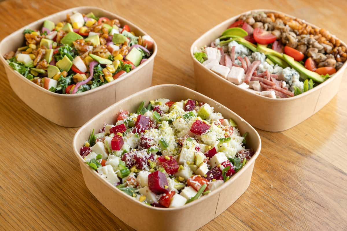 Fresh gourmet salads topped with vegetables, grains, herbs, and protein options, prepared for healthy restaurant catering and takeout dining.