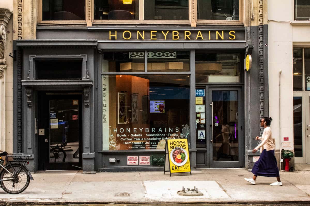 HoneyBrains healthy café storefront with gold signage, large front windows, and sidewalk entrance in a downtown city streetscape.