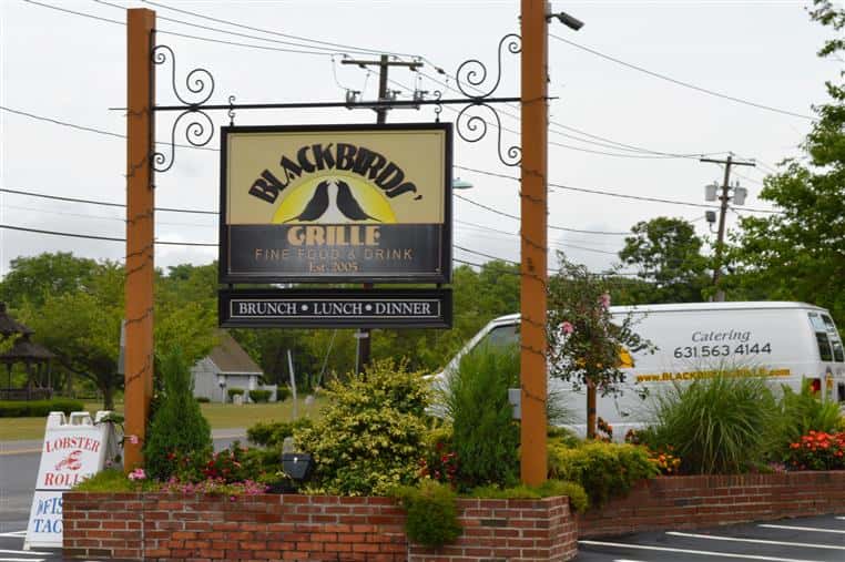 Blackbirds hanging sign over brick planter in parking lot