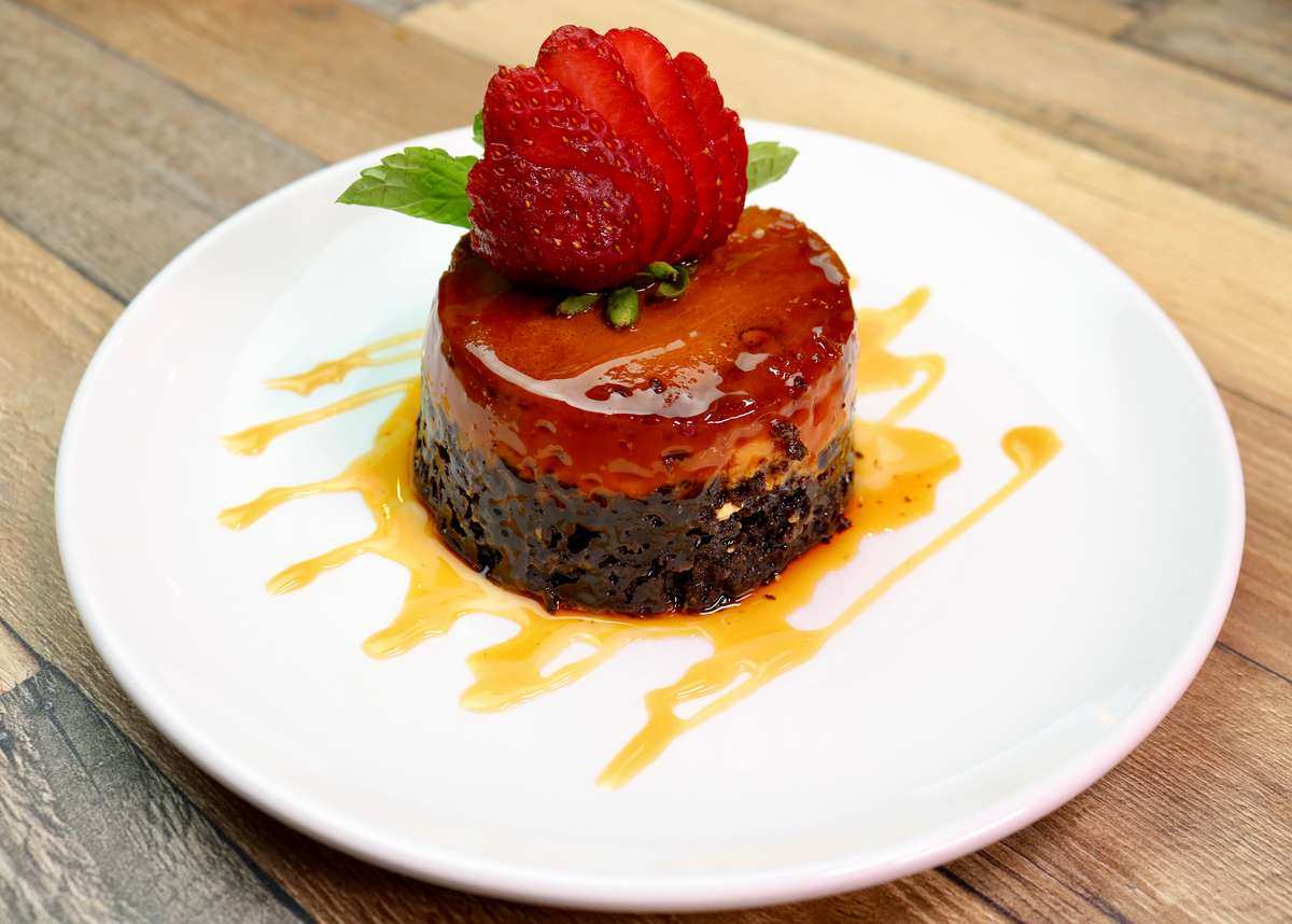 Chocoflan dessert topped with a sliced strawberry and mint leaf, drizzled with caramel sauce on a white plate.