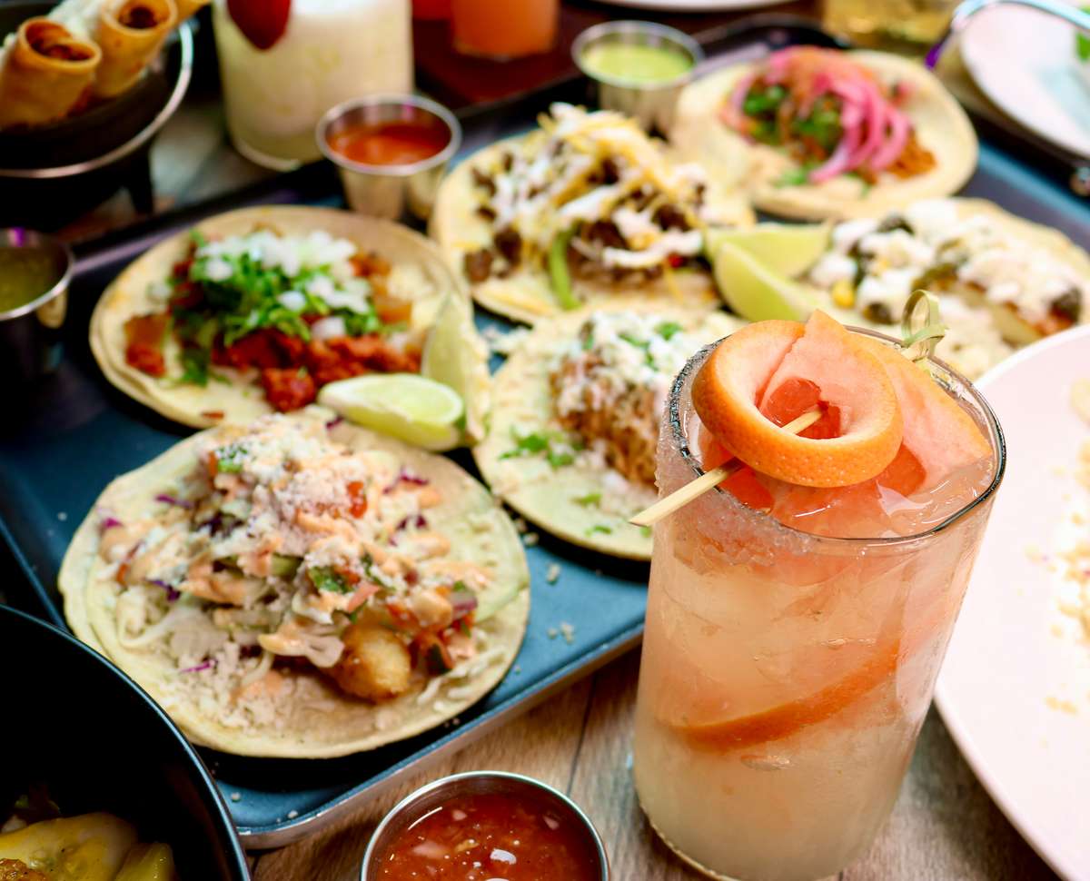 Assorted tacos with various toppings served alongside salsa and a grapefruit cocktail garnished with a citrus twist.