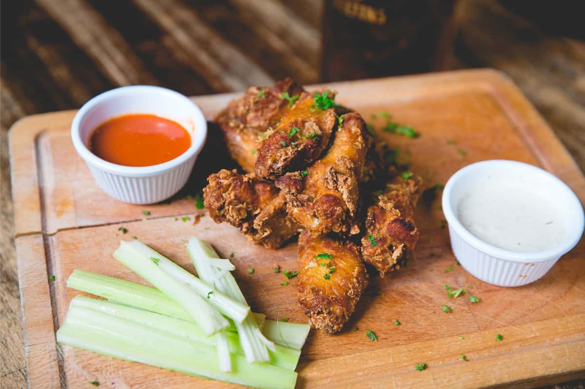 Crispy chicken wings served with celery sticks, buffalo sauce, and ranch dressing on a wooden board at Berliner Pub, perfect for sharing with friends.