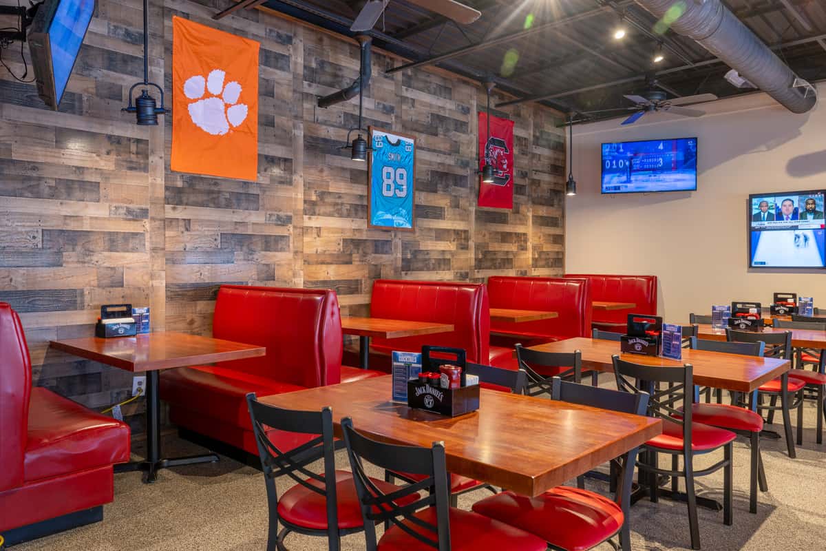 Restaurant booth seating with bright red vinyl benches and wooden tables against a wood-paneled wall, decorated with framed sports jerseys and wall-mounted lights.