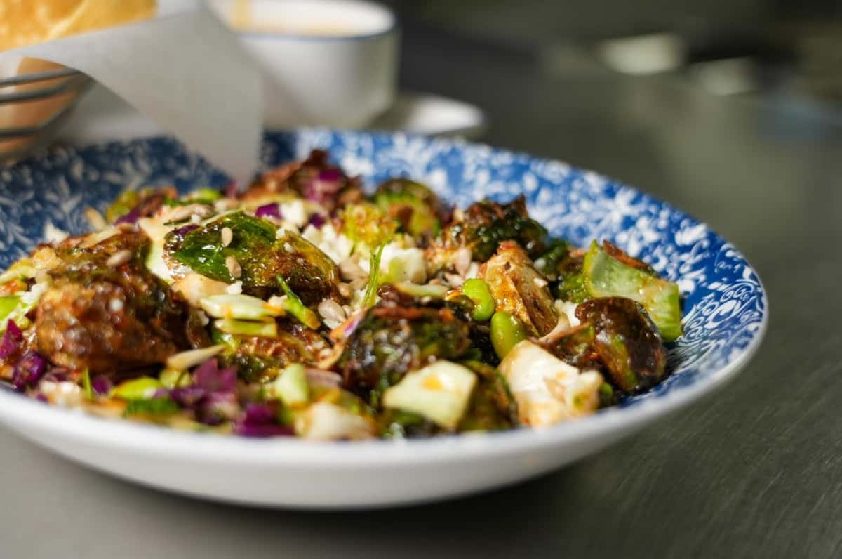 Crispy Brussels sprouts tossed with shredded cabbage, edamame, and a savory glaze, served in a blue patterned bowl.