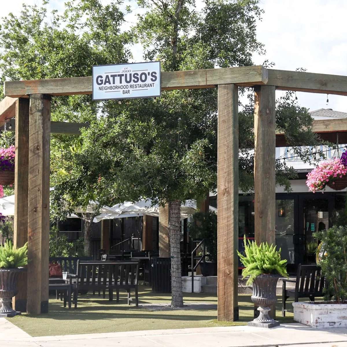 The entrance to Gattuso's Neighborhood Restaurant and Bar, featuring a sign above a wooden structure, with outdoor seating and greenery in the background.