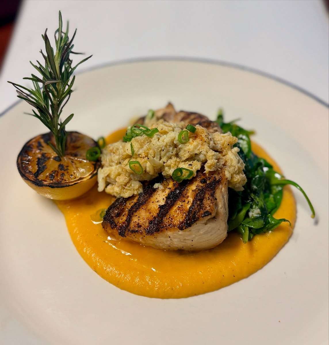 A grilled piece of fish topped with a crab stuffing, served on a bed of spinach, with grilled lemon, rosemary, and a sweet potato puree.