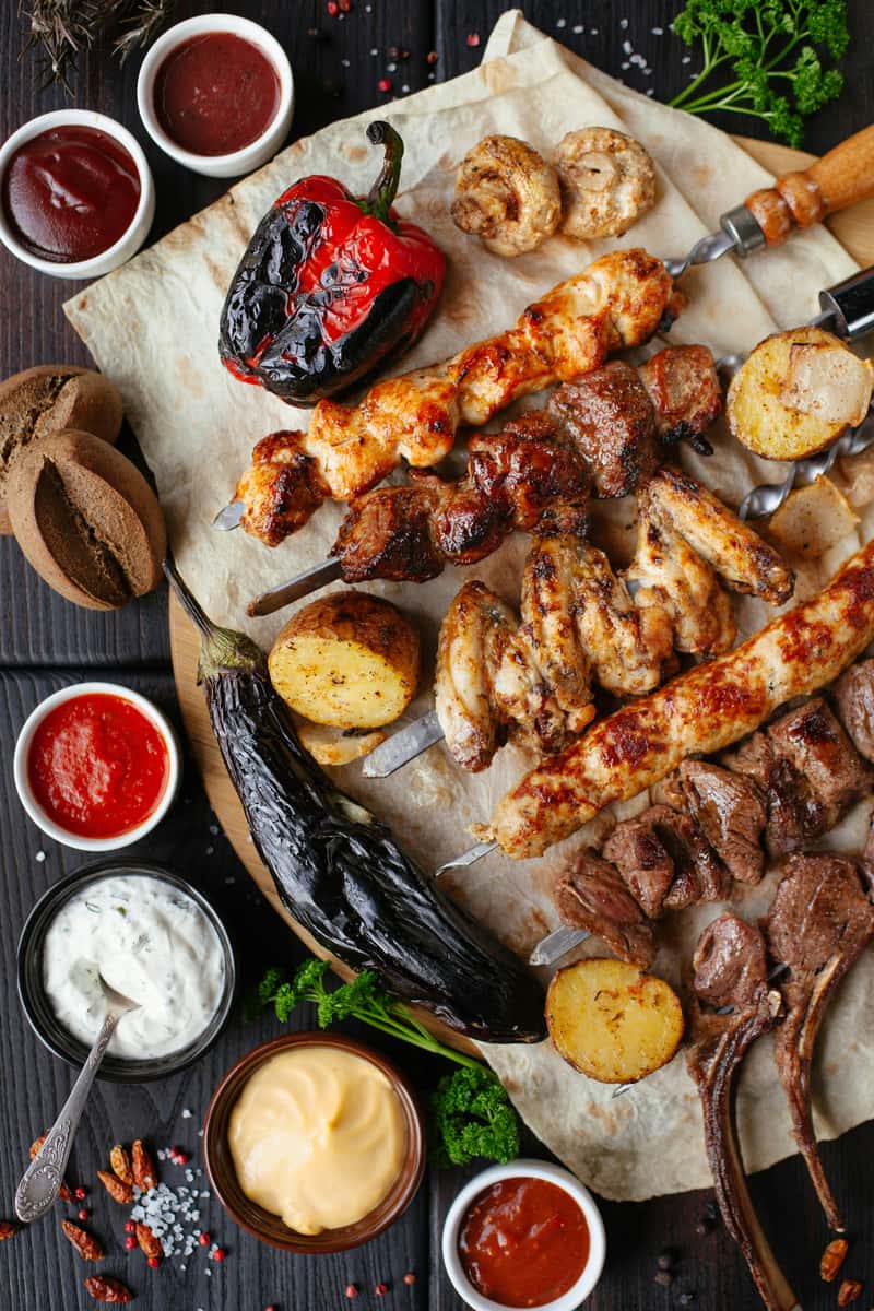 Platter of assorted grilled meats on skewers with roasted vegetables, sauces, and charred bread, ideal for barbecue or Mediterranean-style restaurant presentations.
