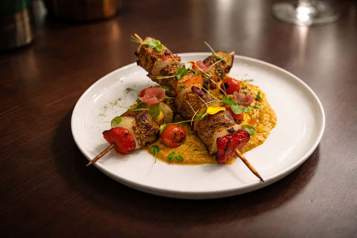Grilled paneer and vegetable skewers with cherry tomatoes and microgreens, served over a spiced lentil or curry puree in a contemporary Indian restaurant.