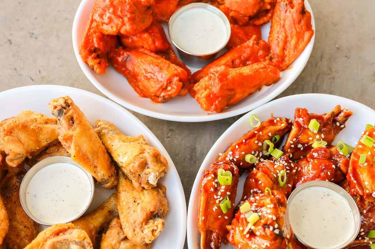 Plates of chicken wings with ranch dip, featuring classic buffalo, plain fried, and sweet spicy wings topped with sesame and scallions.