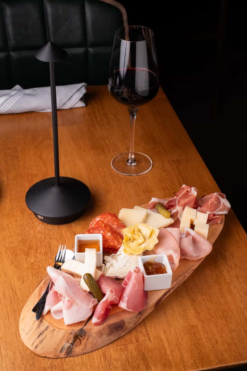 Gourmet charcuterie board with assorted meats and cheeses paired with a glass of red wine on a warm wooden table.