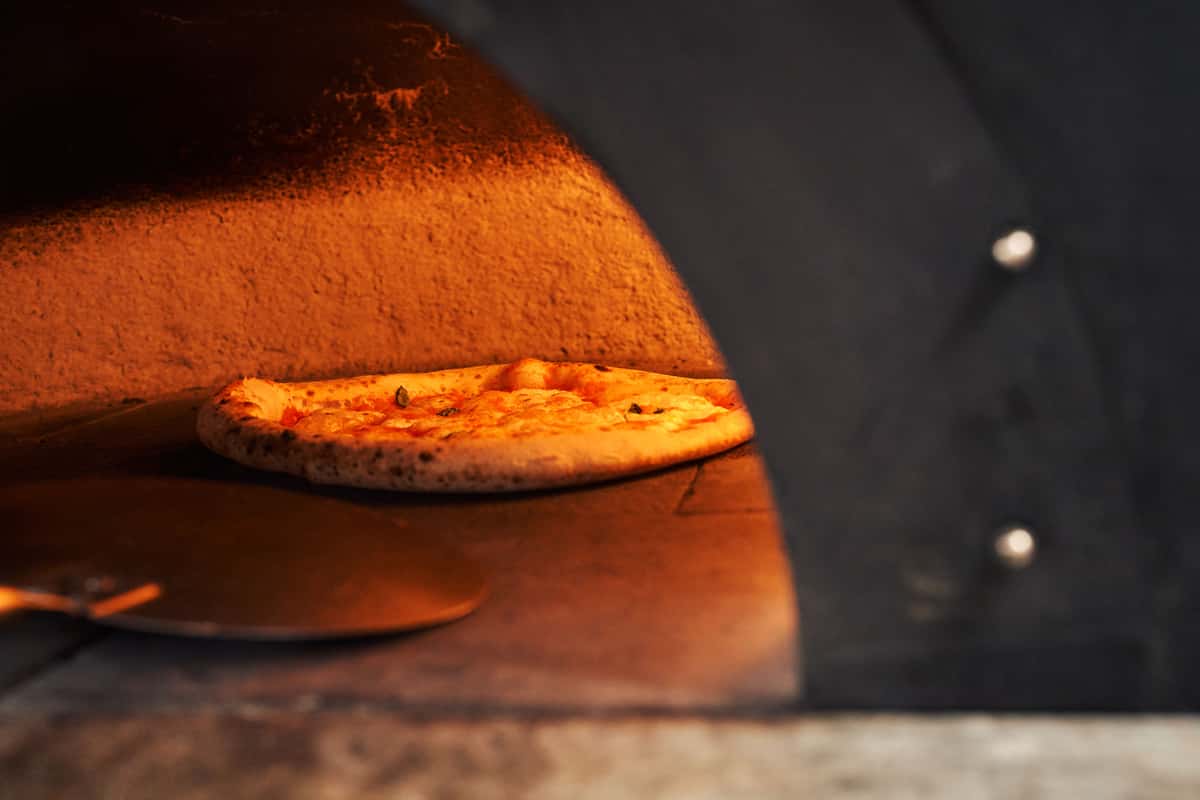 Wood-fired pizza baking in a traditional oven with golden crust