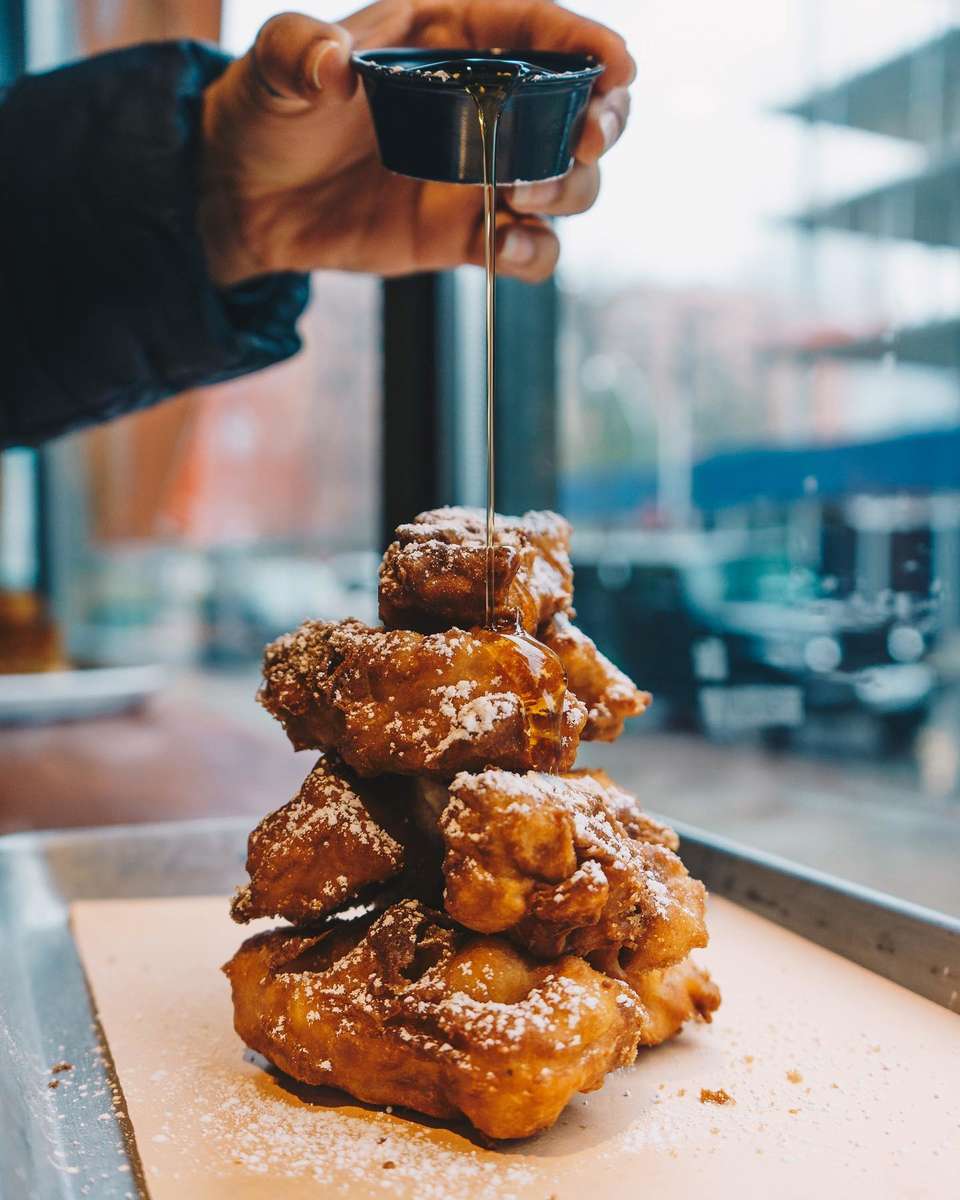 Hand pouring syrup on chicken and waffles
