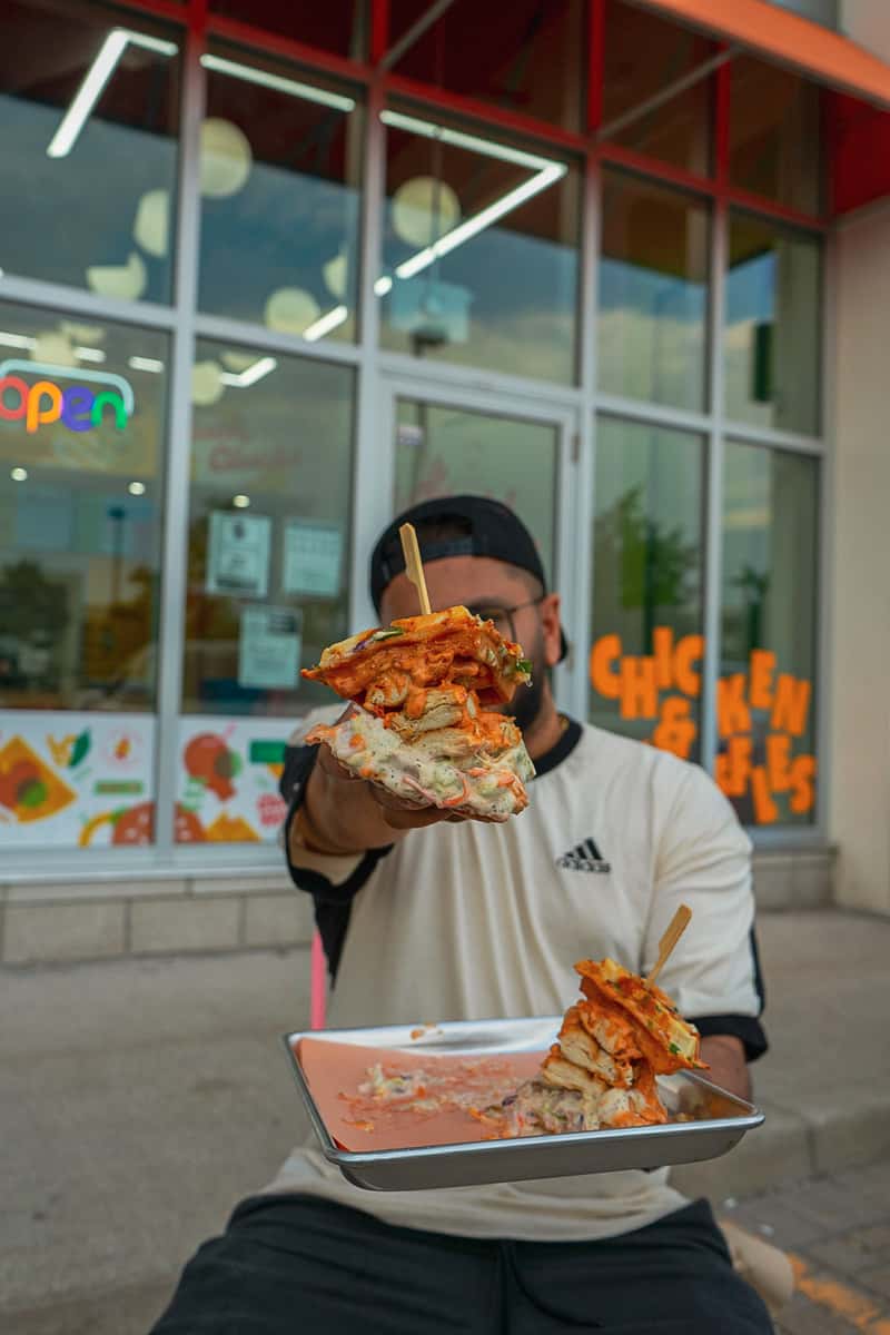 Person holding chicken and waffles sandwich in front of Cluck Clucks