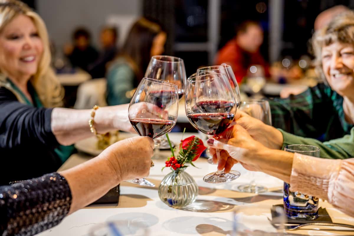 Group of friends toasting with glasses of red wine at a cozy dinner in a casual upscale American restaurant setting.