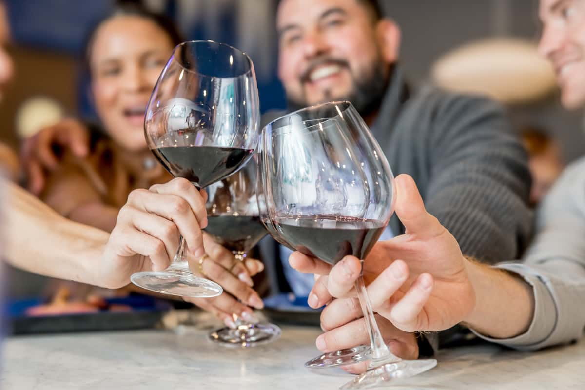 Group of friends clinking glasses of red wine at a bar, smiling and enjoying a cheerful toast together.