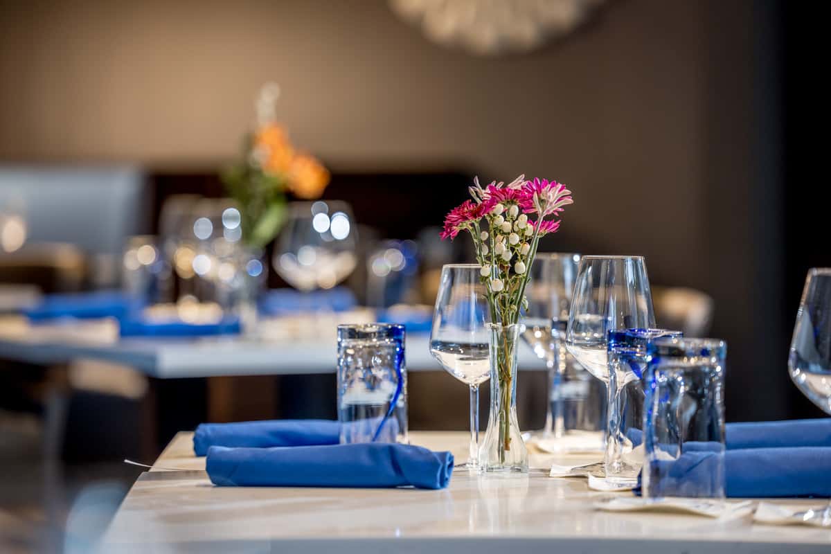 Elegant restaurant table set with blue napkins, wine glasses, and a vase of pink and white flowers, ready for fine dining.