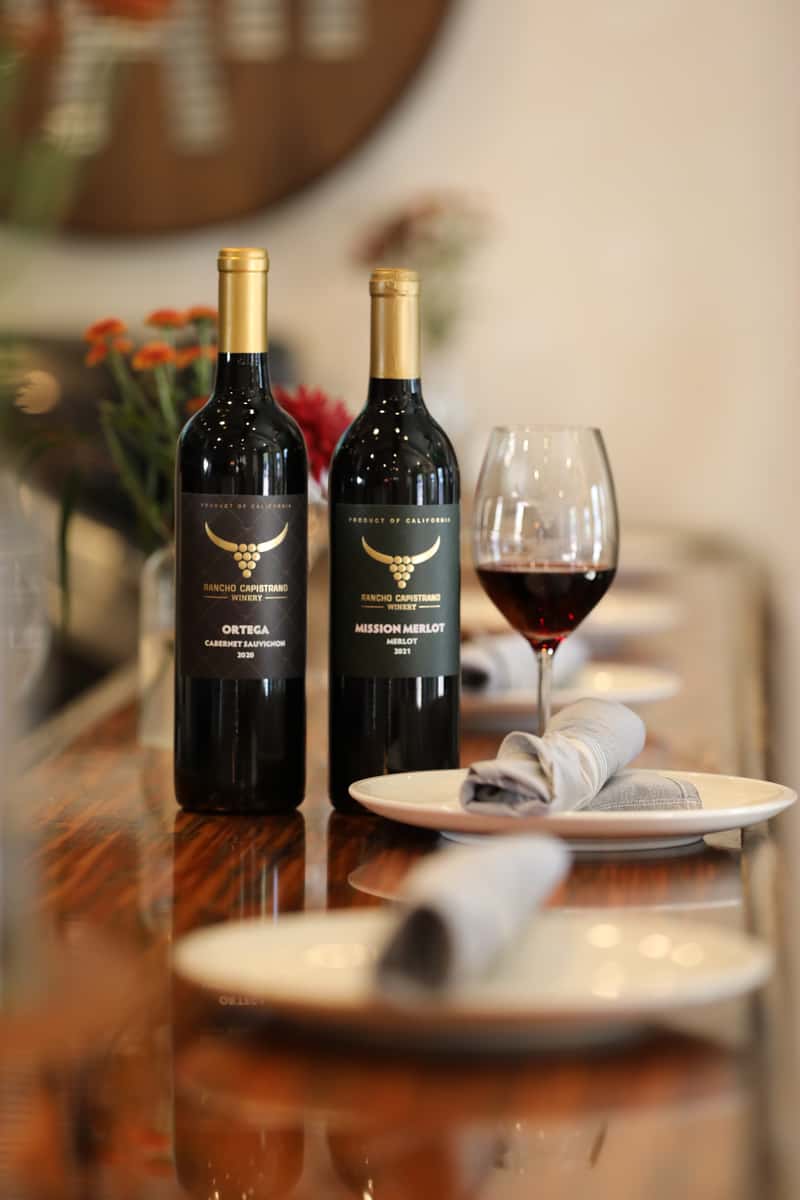Two wine bottles and a wine glass filled with a red wine on a dining table