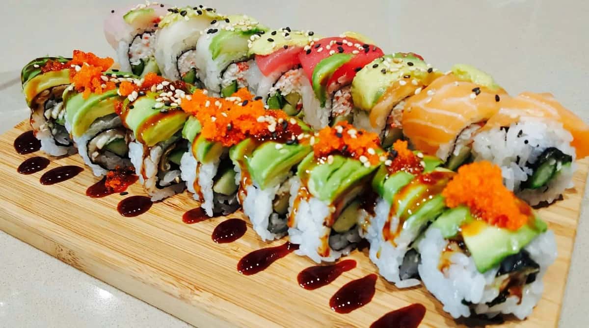 Sushi rolls topped with avocado, sesame seeds, and roe on a wooden board