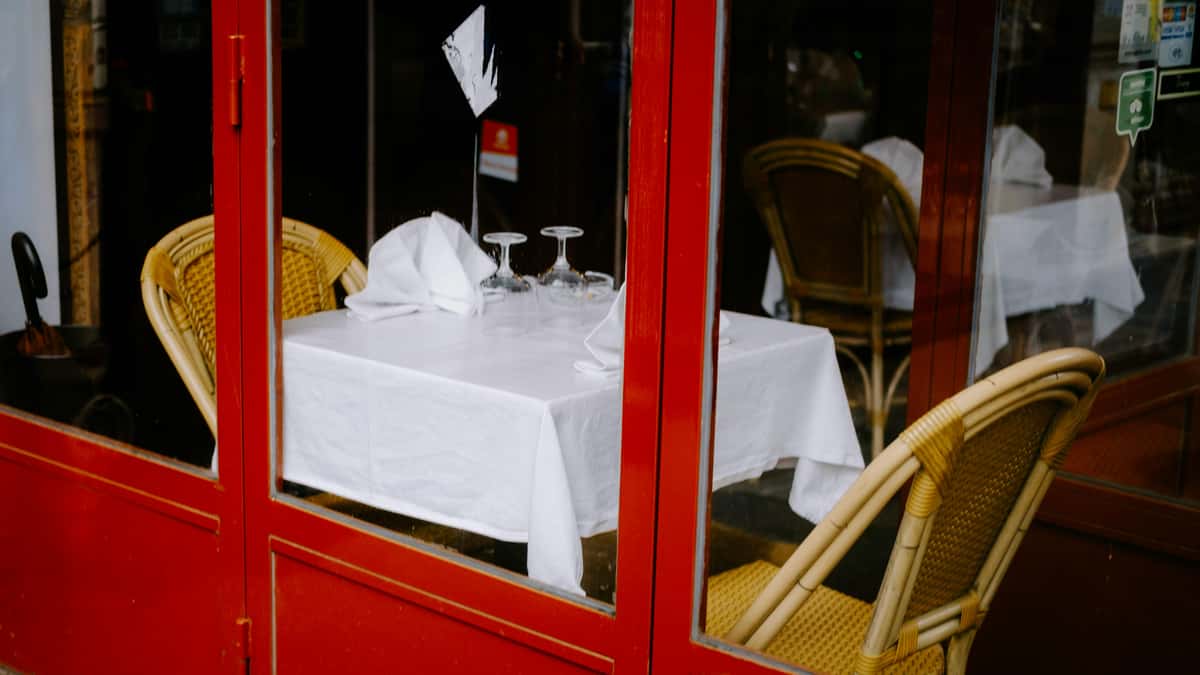 Table setting with white tablecloth and wicker chairs seen through the red framed window of City Limits Bar and Grill.