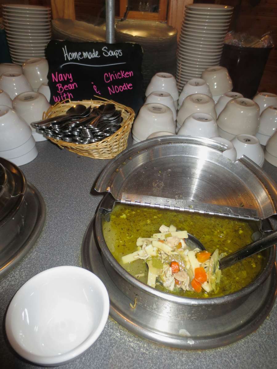 Soup buffet at City Limits Bar & Grill features homemade navy bean and chicken noodle soups, with white bowls and stacked plates.