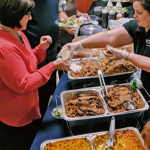 rays of barbecue pork and mac and cheese being served at a party