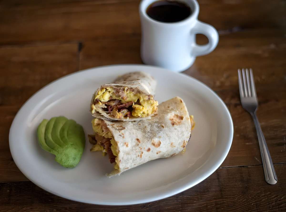 Breakfast burrito served with sliced avocado and salsa.