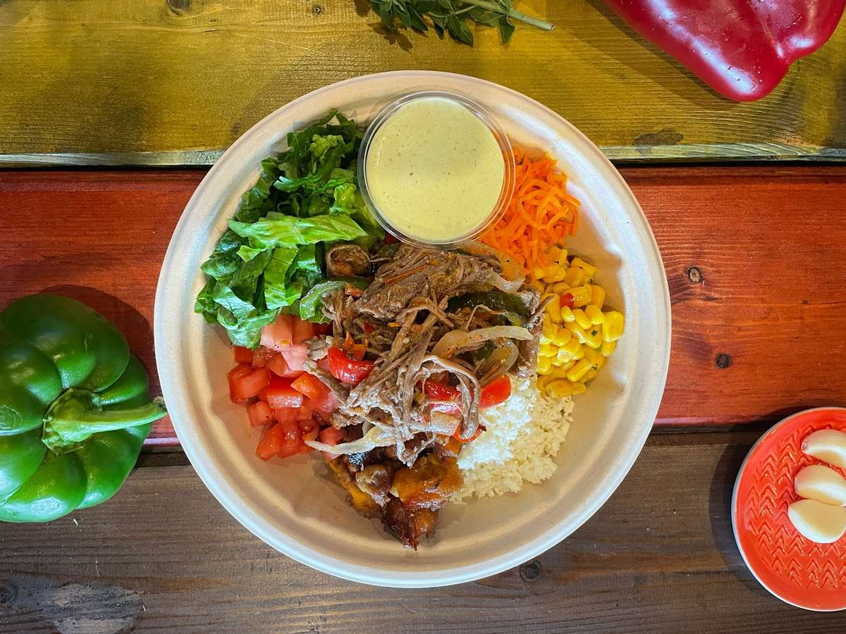 Latin rice bowl with shredded beef, white rice, corn, tomatoes, lettuce, and creamy dressing on rustic table