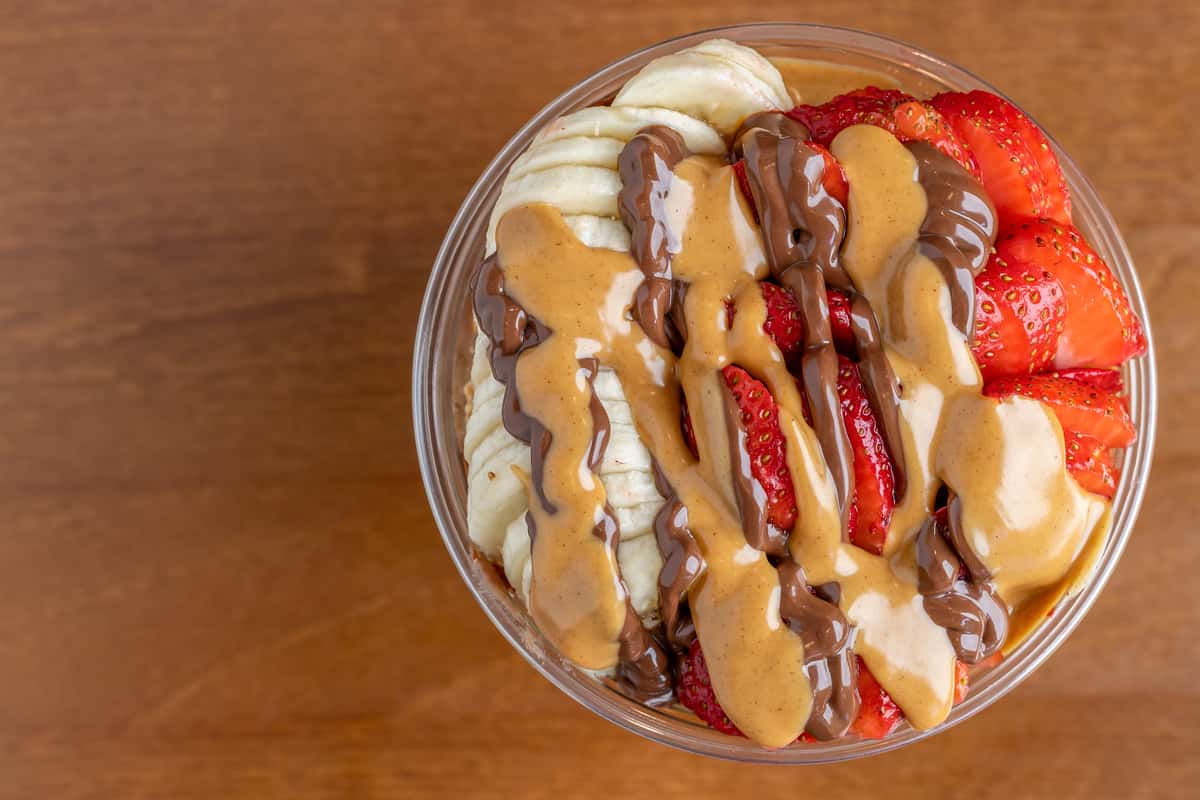 Sliced bananas and strawberries topped with peanut butter and chocolate drizzle in a smoothie or acai bowl.