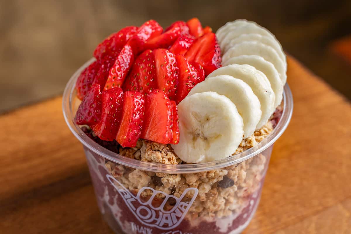 Acai bowl topped with fresh sliced strawberries and bananas on a wooden table.