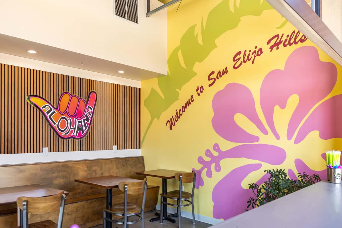 ALOHAHA shop interior with colorful wall art, wooden seating, and a vibrant "Welcome to San Elijo Hills" hibiscus mural.