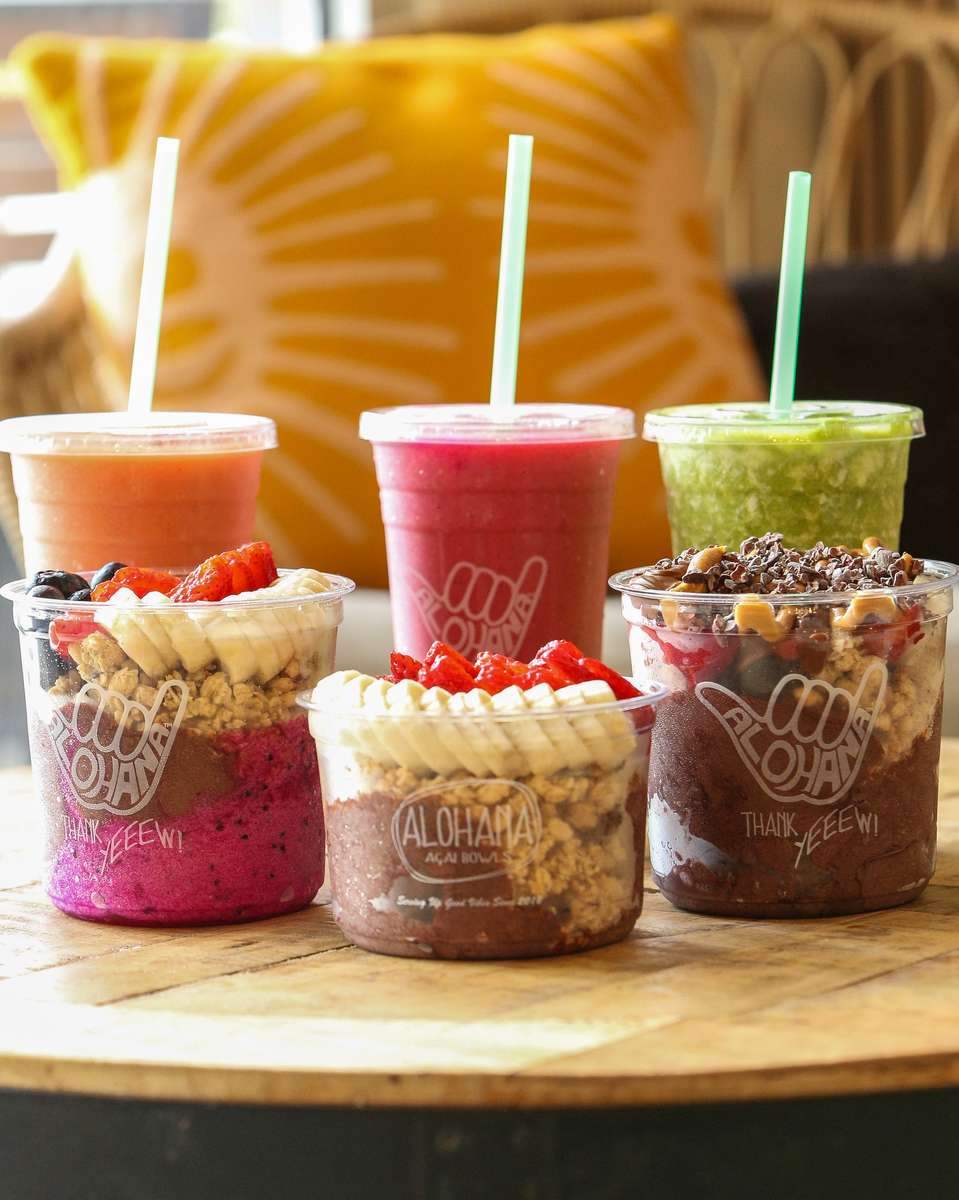 A variety of ALOHANA Acai Bowls and smoothies on display, featuring acai bowls topped with granola, fruits, and colorful smoothies with straws.