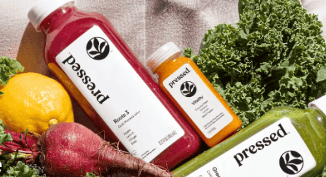 Bottles of Pressed juices surrounded by fresh kale, lemon, and beets, featuring vibrant red, orange, and green juice blends.