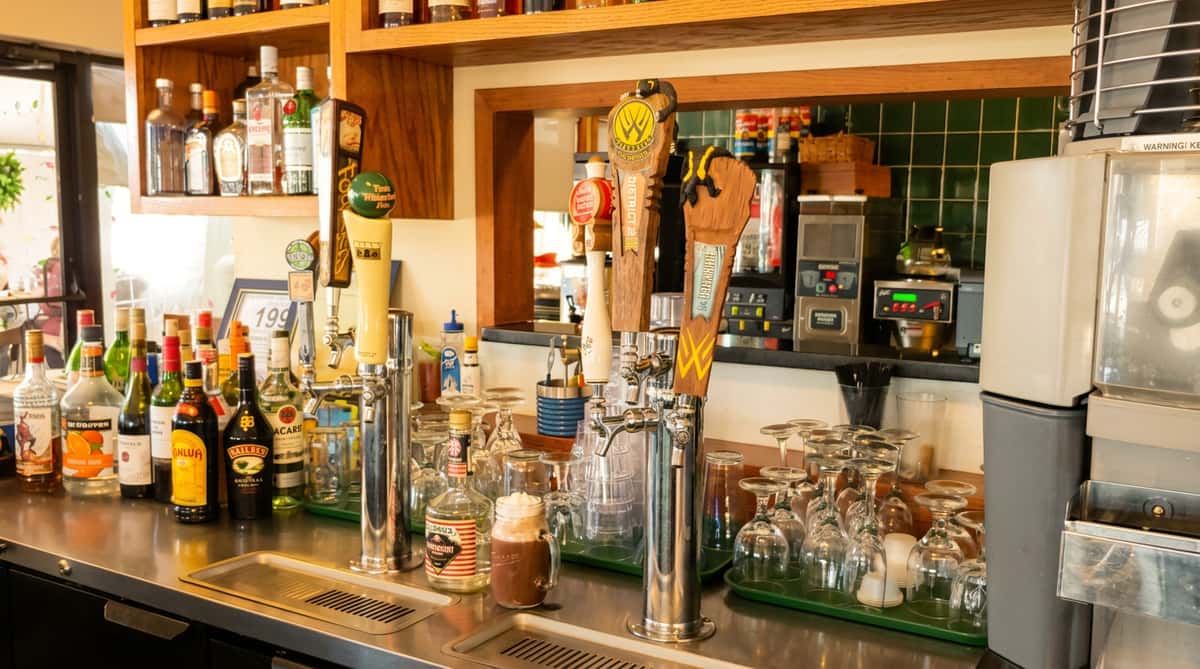 A bar counter with liquor bottles, beer taps, glassware, and a cocoa drink with whipped cream.