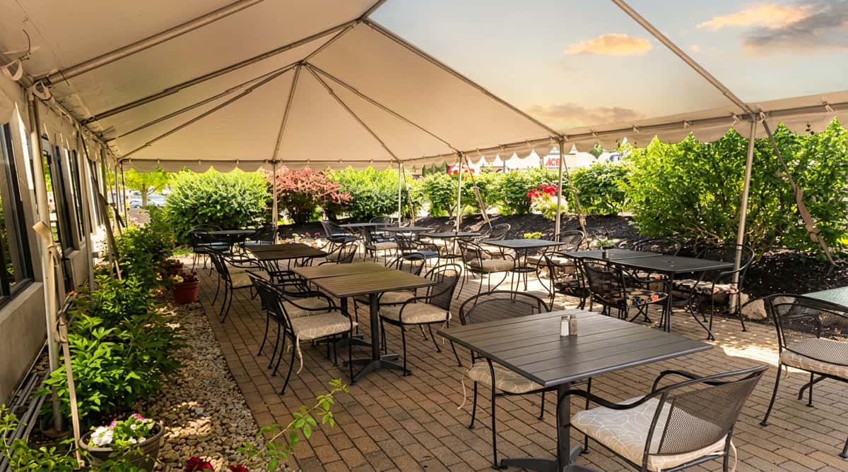 Outdoor patio dining area under a white tent with black metal tables and chairs on a brick paver floor.